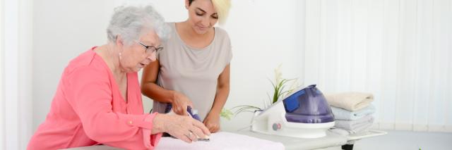 Eine junge Frau hilft einer älteren beim Bügeln.