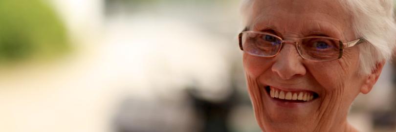 Seniorin lächelt zufrieden und zeigt dabei ihre schönen dritten Zähne (Zahnersatz).