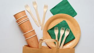 Becher, Teller und Servietten aus Papier und Besteck aus Holz über einer Papiertüte